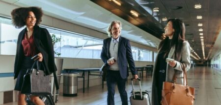 Three smiling airport passengers walk together inside a terminal.