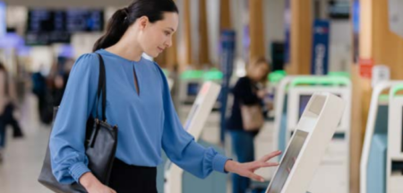 A woman in blue uses a biometric check-in kiosk.