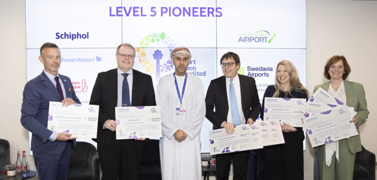 Six airport executives stand in front of ACI Europe's sign that says "Level 5 Pioneers".