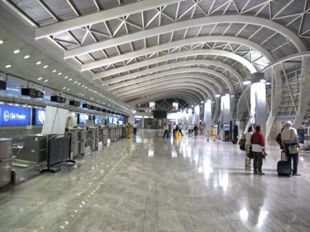 The inside of an airport terminal, with check-in desks to the left and passengers to the right.