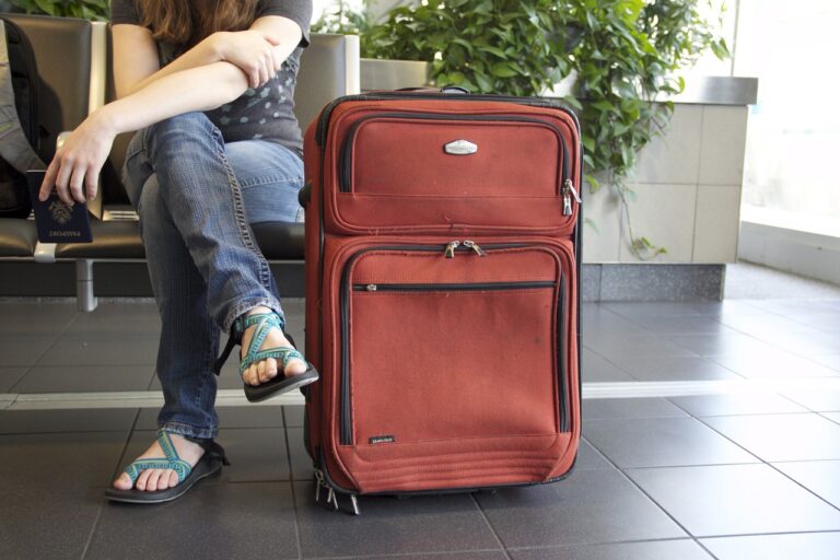 A large red suitcase sits next to a sitting passenger's crossed legs.