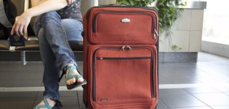 A large red suitcase sits next to a sitting passenger's crossed legs.