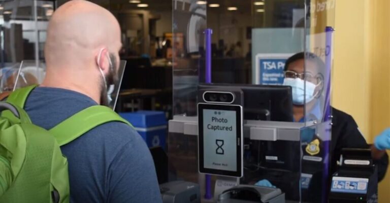 US Department of Homeland Security releases first AI roadmap An airport staff member in a face mask watches as a passenger has his photo scanned before boarding.