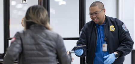 A smiling TSA officer hands back a passenger’s passport.