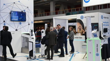 A Vision-box booth at a trade show, surrounded by executives in suits chatting.