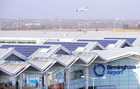 A view of Birmingham Airport's roofs and solar panels with a plane taking off in the background.