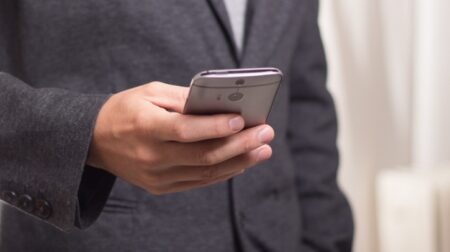 A man in a suit holds a smartphone in his right hand.