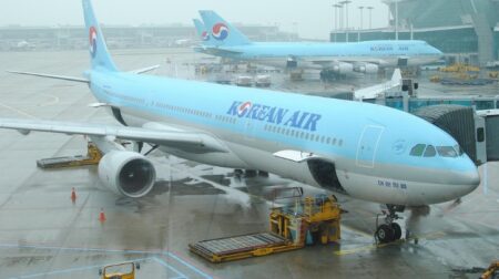 Two planes with the words "Korean Air" sit parked outside an airport.