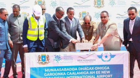 A group of executives collectively lay a foundation stone next to a banner, which trans-lates to "Groundbreaking Ceremony New Mogadishu Airport".
