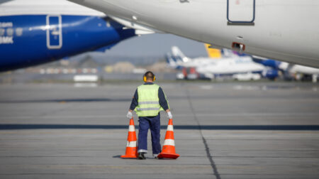 Civil Aviation Authority of Singapore to invest S$200m in workforce development A man holding two traffic cones walks beneath a commercial airplane