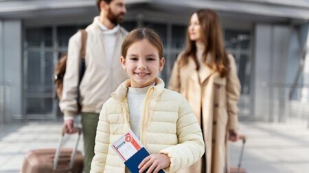 A child clutching a passport and smiling at the camera is followed by two adults, who are locked in conversation