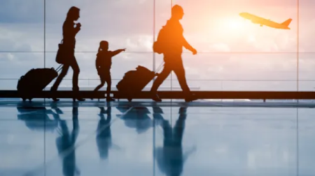 Two parents and a child walk through an airport terminal concourse as the sun sets behind them and a plane takes off on the distance