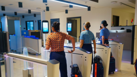 Three passengers scan their faces at a biometric gate.