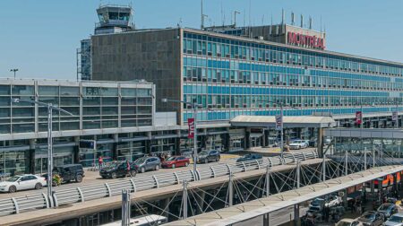An extrenal image of Montral airport with drop-off points out the front. Cars and buses are passing.