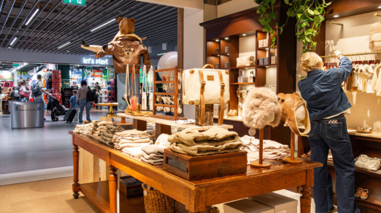 A staff member in a denim jacket and jeans organises clothing on a rail in the new Donsje Amsterdam store at Schiphol airport