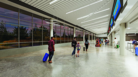 Passengers walk along a terminal concourse in an airport, pulling wheeled luggage