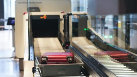 A piece of red carry-on luggage in a tray going through a CT scanner at an airport