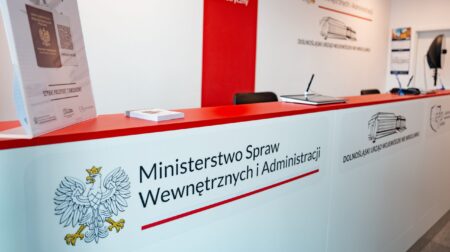 A white customer service desk with a red top and a red line on the wall behind, at the new passport issuance facility at Wrocław Airport
