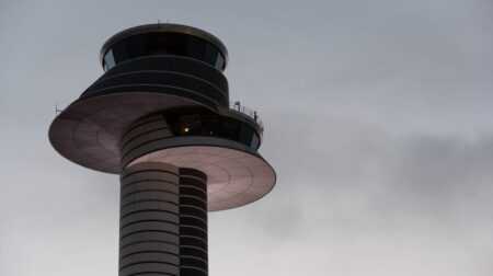 An air traffic control tower against a grey, cloudy sky