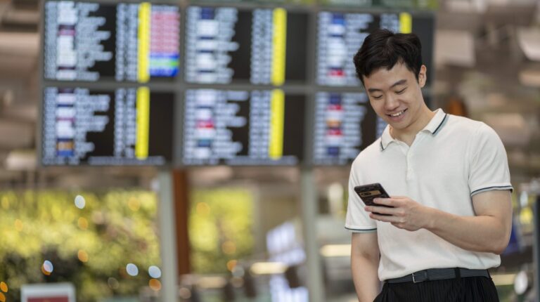 A passenger at Changi Airport checks their phone in front of a large information screen
