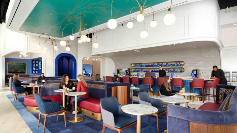 JetBlue launches first lounge at JFK Terminal 5 JetBlue's first lounge, BlueHouse, at JFk airport in New York City. Ther is a blue carpet floor, blue-backed chairs and a green ceiling with a white serving area. Dark blue trim features around doorways in the background