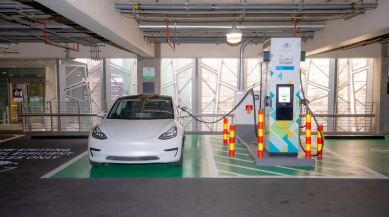 A white sports car is plugged into an electric vehicle charging point in a car park.