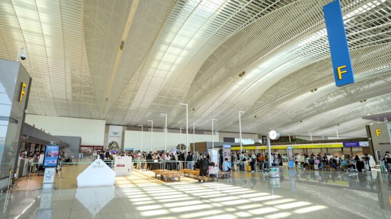 Check-in hall at Incheon airport, with a high ceiling with multiple large windows, check-in counters, and passengers standing in short queues.