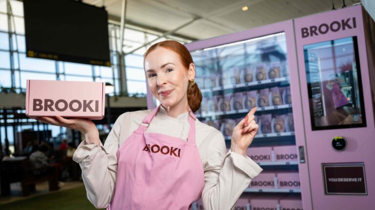 Brooki Bakehouse launches first cookie vending machine at Brisbane Airport Brooki Bakehouse founder Brooke Bellamy poses in front of the new cookie vending machine at Brisbane Airport, wearing a pink apron and holding a matching pink Brooki cookie box.