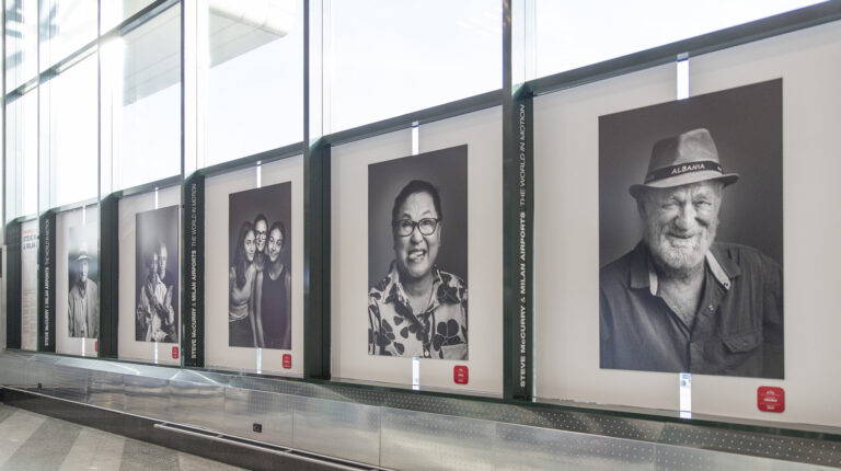 The Steve McCurry photography exhibition at Milano Malpensa airport, featuring black and white portraits of passengers from around the world, for Milan-Cortina 2026.