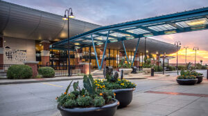 Entrance to Lexington Blue Grass Airport. The airport name is written to the left or the large entrance doors and a glass canopy extends out to offer protection from the elements. The sun is low in the sky.