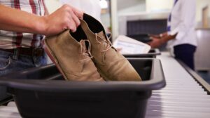Man putting shoes into tray for airport security check.