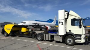 A Hyzon hydrogen-powered truck parked on the airport tarmac at Kaunas Airport in front of a large airplane.