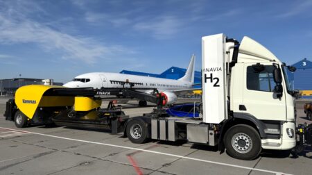 A Hyzon hydrogen-powered truck parked on the airport tarmac at Kaunas Airport in front of a large airplane.