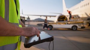 Member of ground crew preparing airplane before flight. Worker using tablet against plane at airport.