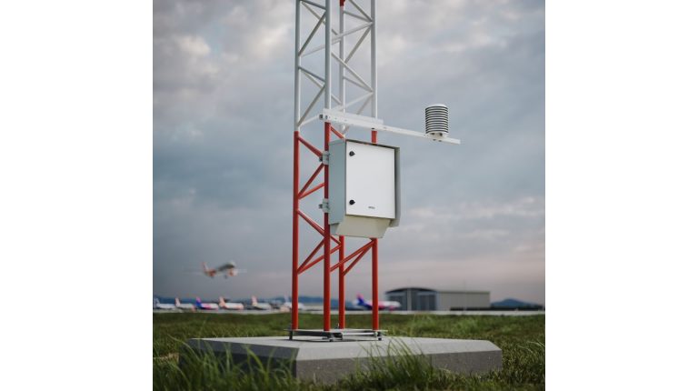The Vaisala AWS810 Airport Edition automatic weather station in operation at an airport, with aircraft taxiiing along the runway in the foreground and background under a cloudy grey sky.