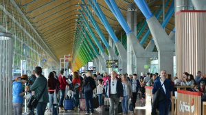 Passengers stand in a queue on an airport concourse.