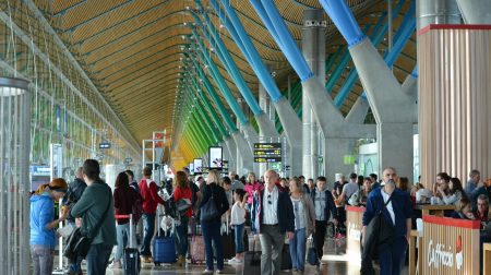 Passengers stand in a queue on an airport concourse.