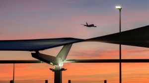 A plane takes off at an airport at night time as the sun sets. Airport infrastructure is visible in silhouette in the foreground.