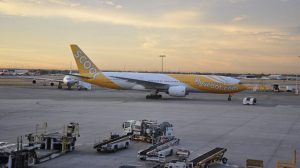A white and yellow Scoot airplane taxis across the tarmac at Perth Airport.