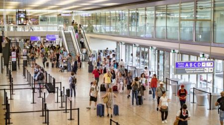 Concourse at Geneve Airport, with passengers moving to their gates. There is an escalator and stairs to an upper level.