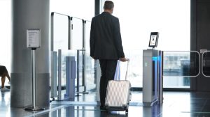 A male pasenger in a dark suit pulls a small suitcase through passenger check-in.