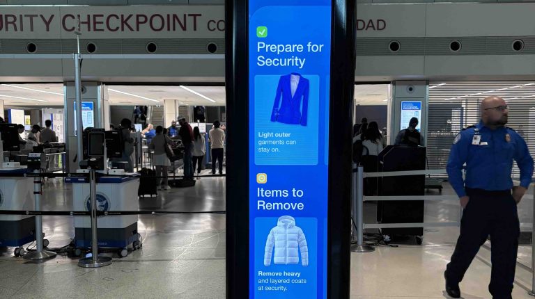 A blue dynamic digital displays at a TSA checkpoint at an airport, displaying passenger information.