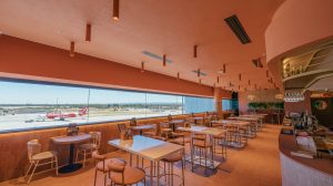 Co + Co at Perth Airport T1 International terminal. It has a wooden tables and chairs, a long window with views of the runways, and hanging lights.