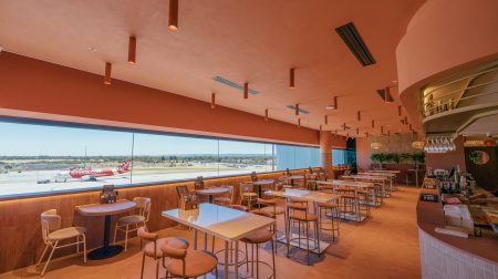 Co + Co at Perth Airport T1 International terminal. It has a wooden tables and chairs, a long window with views of the runways, and hanging lights.