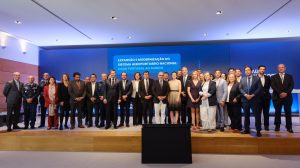 Official representatives of Vinci Airports stand on a stage in front of a screen to mark the submission of the report for new Lisbon airport project.