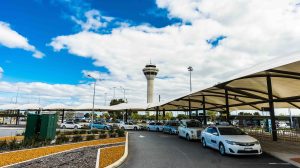 External front entrance to Perth Airport with a line of taxis and a blue sky with some clouds.