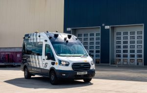An Aurrigo SENTRY autonomous vehicle parked outside a warehouse or industrial facility.