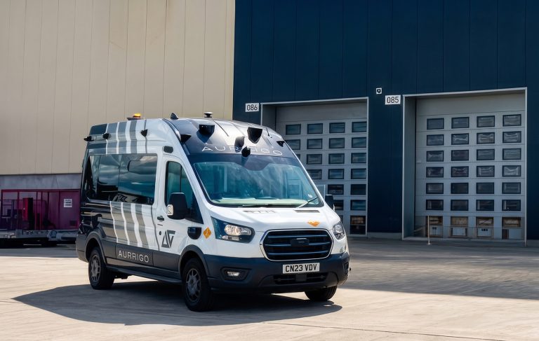 An Aurrigo SENTRY autonomous vehicle parked outside a warehouse or industrial facility.