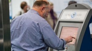 A passenger interacts with a touchscreen Global Entry check-in system at an airport.