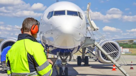 Ground handler using tablet on airport apron with aircraft in background